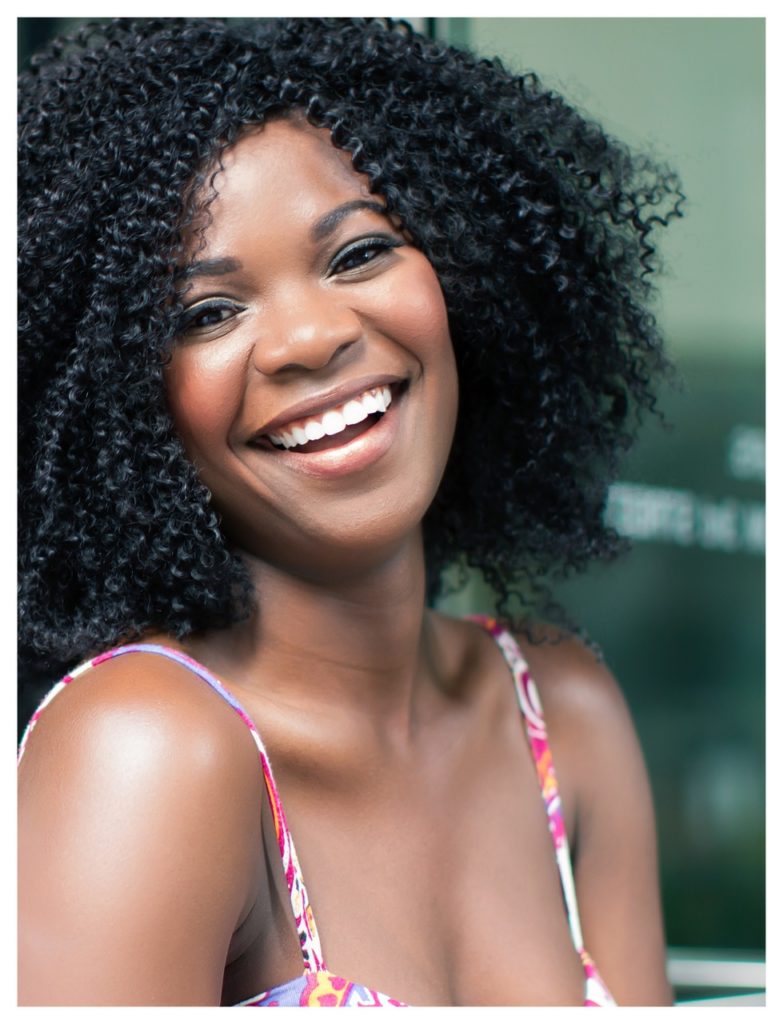 A woman with short, curly black hair, smiling brightly.