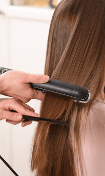A close-up of a woman using a flat iron on her hair.
