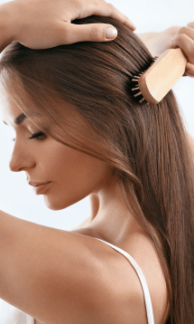 A woman brushing her long straight brown hair with a hairbrush.