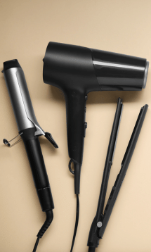 A blow dryer, curling iron, and flat iron laid out on a table.