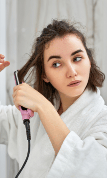 A woman with brown hair using a pink hair straightener.