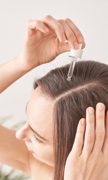A person applying a hair serum or oil to their scalp using a dropper.