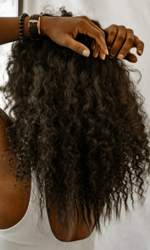 A close-up of a person with thick, curly black hair, being styled.