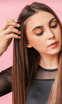 A woman with straight brown hair, touching her hair and looking down.