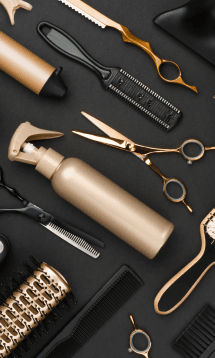 A set of hairstyling tools, including scissors, a comb, and a spray bottle, laid out on a black surface.